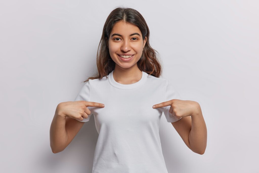 Brunette Latin woman confidently points at blank space on her tshirt inviting creativity and