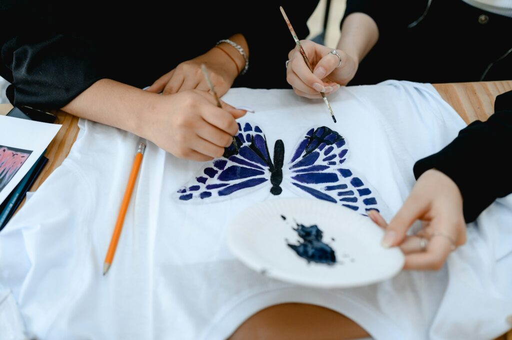 a woman sits at a table and paints a fashionable print on a white t-shirt