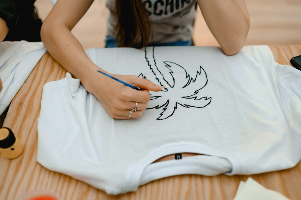a woman sits at a table and paints a fashionable print on a white t-shirt