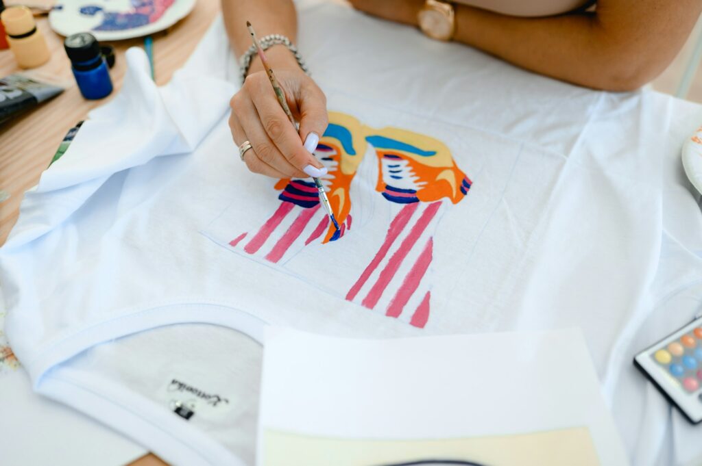 a woman sits at a table and paints a fashionable print on a white t-shirt