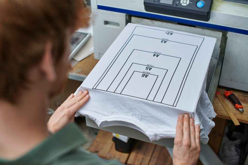 High angle view of young blurred craftsman working with t-shirt with marking and screen printing